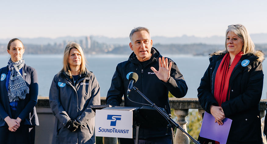 Dow Constantine speaking outside with microphone, with Sound Transit logo visible.