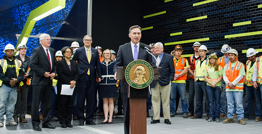 Dow Constantine speaking at a podium in front of a new Light Rail station in 2015.