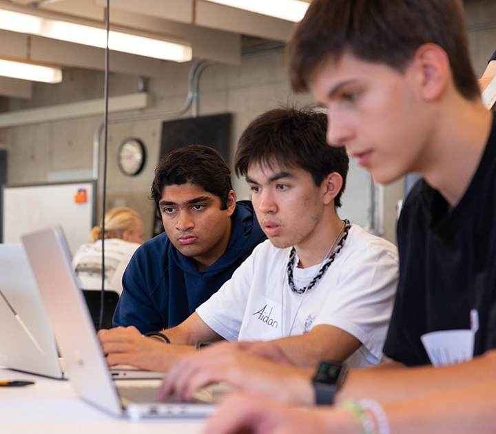 Three UW students sit close together looking at their laptops