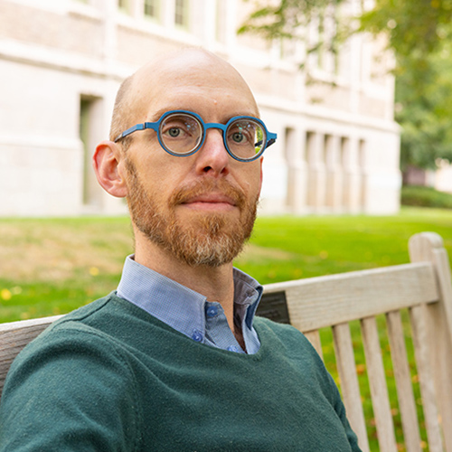 Colin Marshall sitting on a wooden bench on the UW campus.
