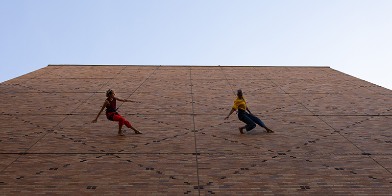 Two dancers dance along the side of Meany Hall. 