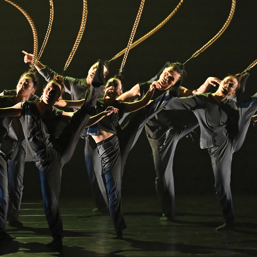 Dancers in black, lifting their leg high in the air